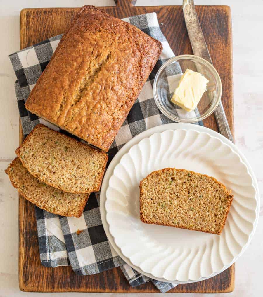 top view of a loaf and slice of banana bread next to a slice of bread on a plate and a bowl of butter