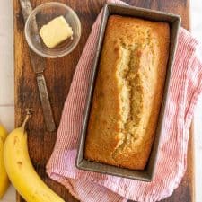 Top view of banana bread next to a banana and a bowl of butter