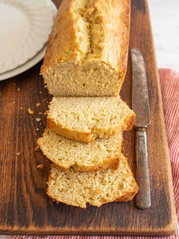 slices of banana bread and a loaf on a cutting board with a butter knife next to the loaf