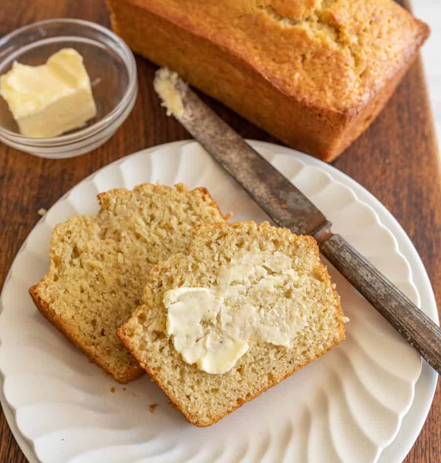 close up of slices of buttered banana bread on a plate with a knife next to them