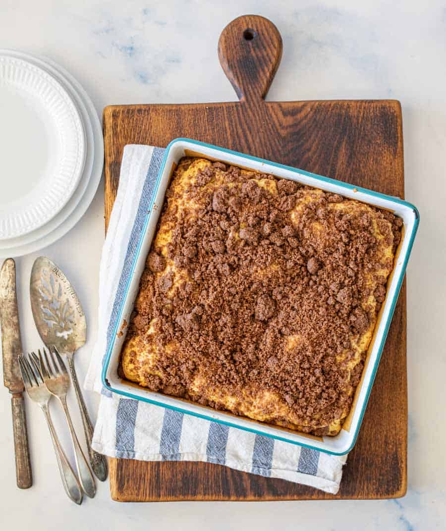 a pan for coffee cake sitting on top of a blue and white striped hand towel on top of a dark wood cutting board