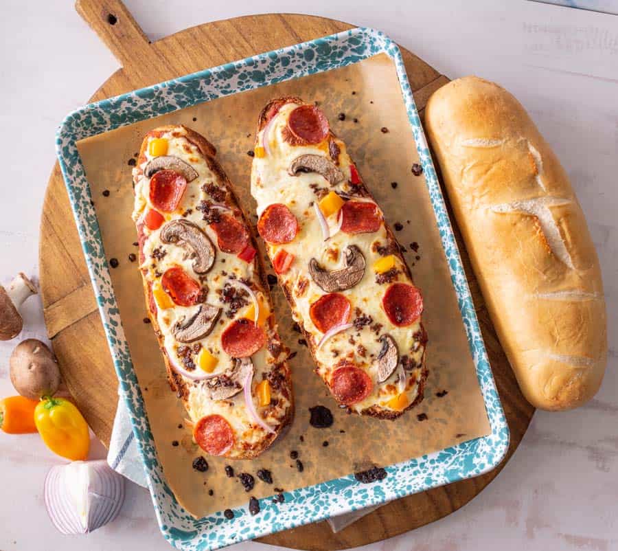 top view of French bread pizza on a baking sheet next to a loaf of bread