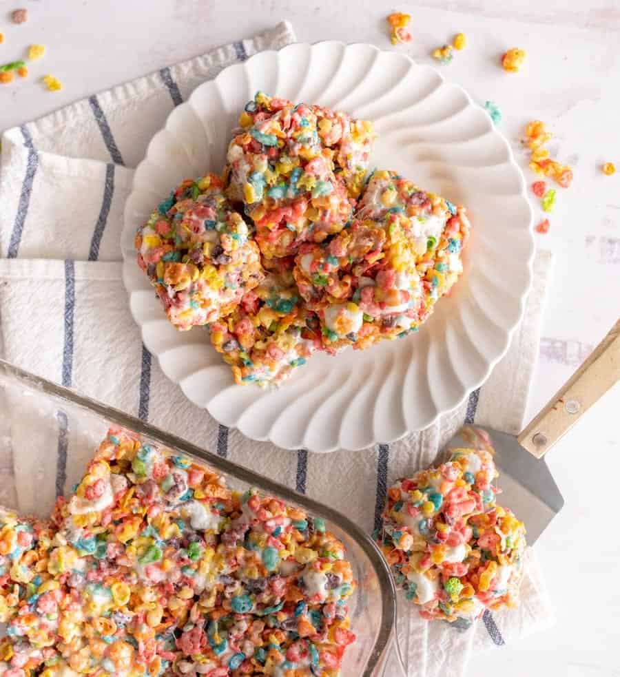 top view of a plate of fruity pebble squares on a plate next to a pan of fruity pebble treats with one on a spatula