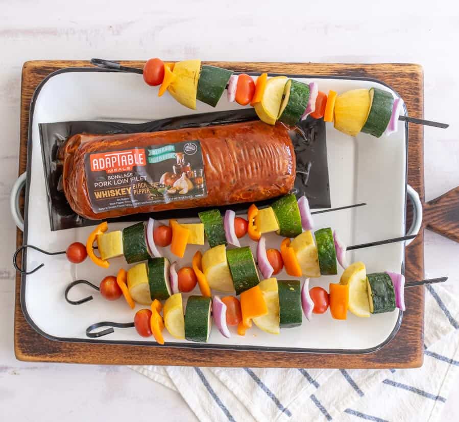 uncooked pork loin in the packaging with uncooked veggie skewers on either side