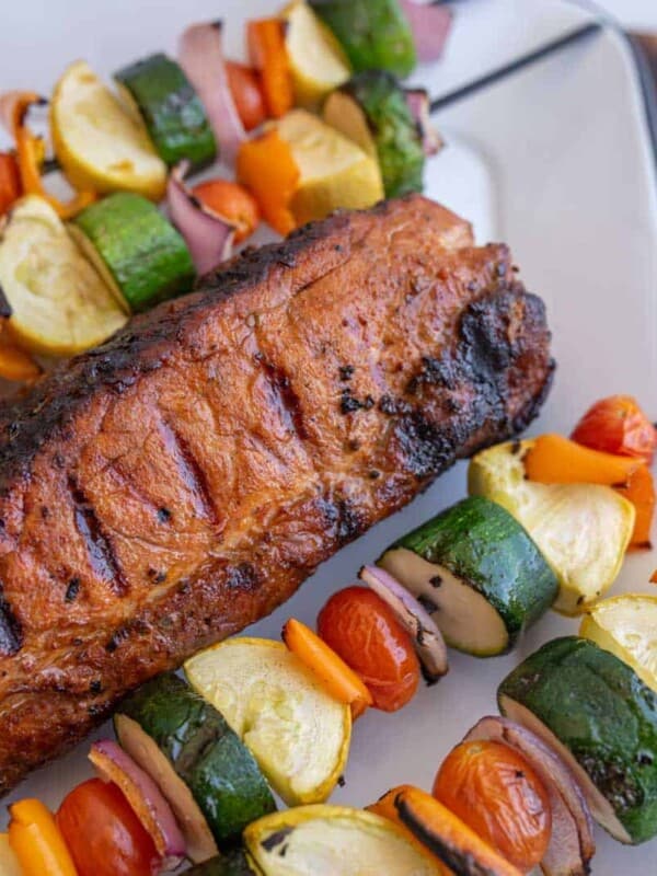 close up picture of a grilled pork loin with grilled vegetable kabobs next to it