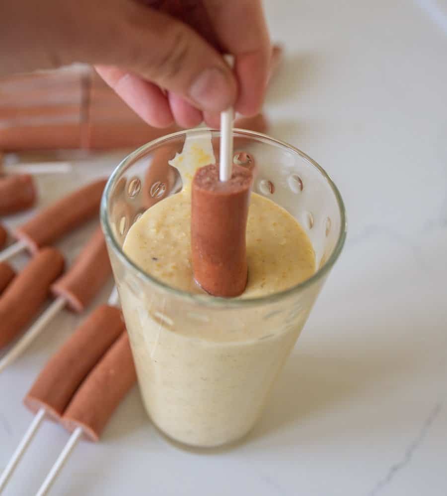 hot dog being dipped in batter to make corndogs