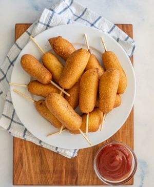 top view of a plate of corndogs with a bowl of ketchup next to it