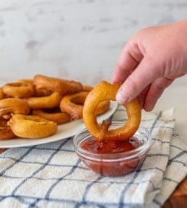 hand dipping onion ring in ketchup.