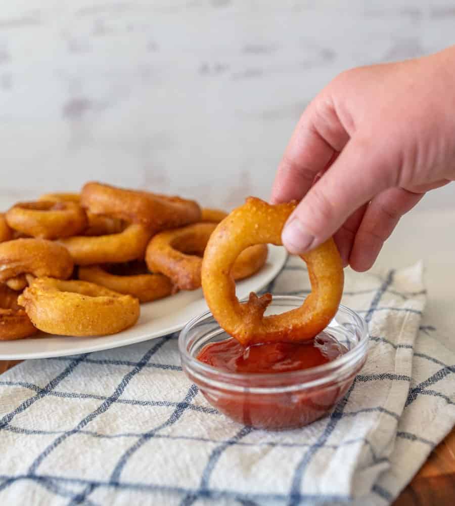 hand dipping onion ring in ketchup
