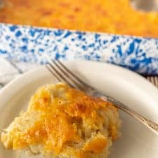 cheesy potato casserole on a plate with a fork and the baking dish in the back