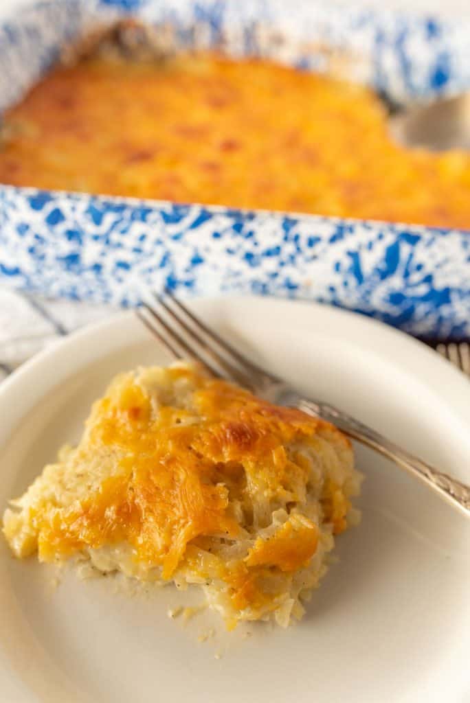 cheesy potato casserole on a plate with a fork and the baking dish in the back