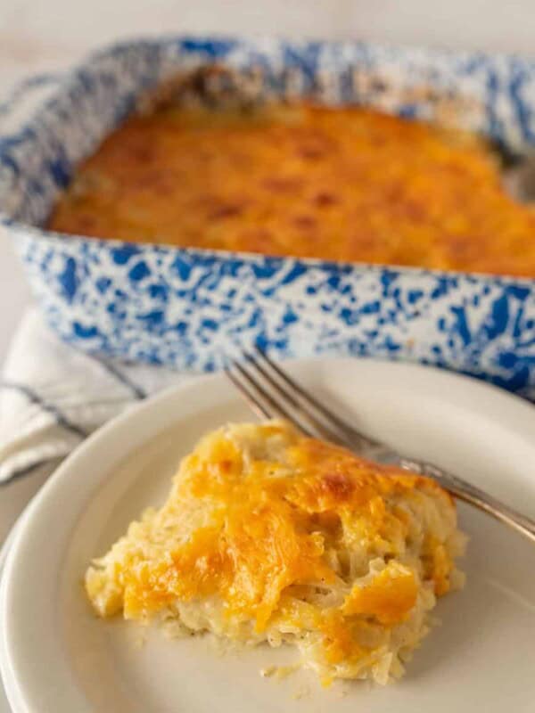 cheesy potato casserole on a plate with a fork and the baking dish in the back