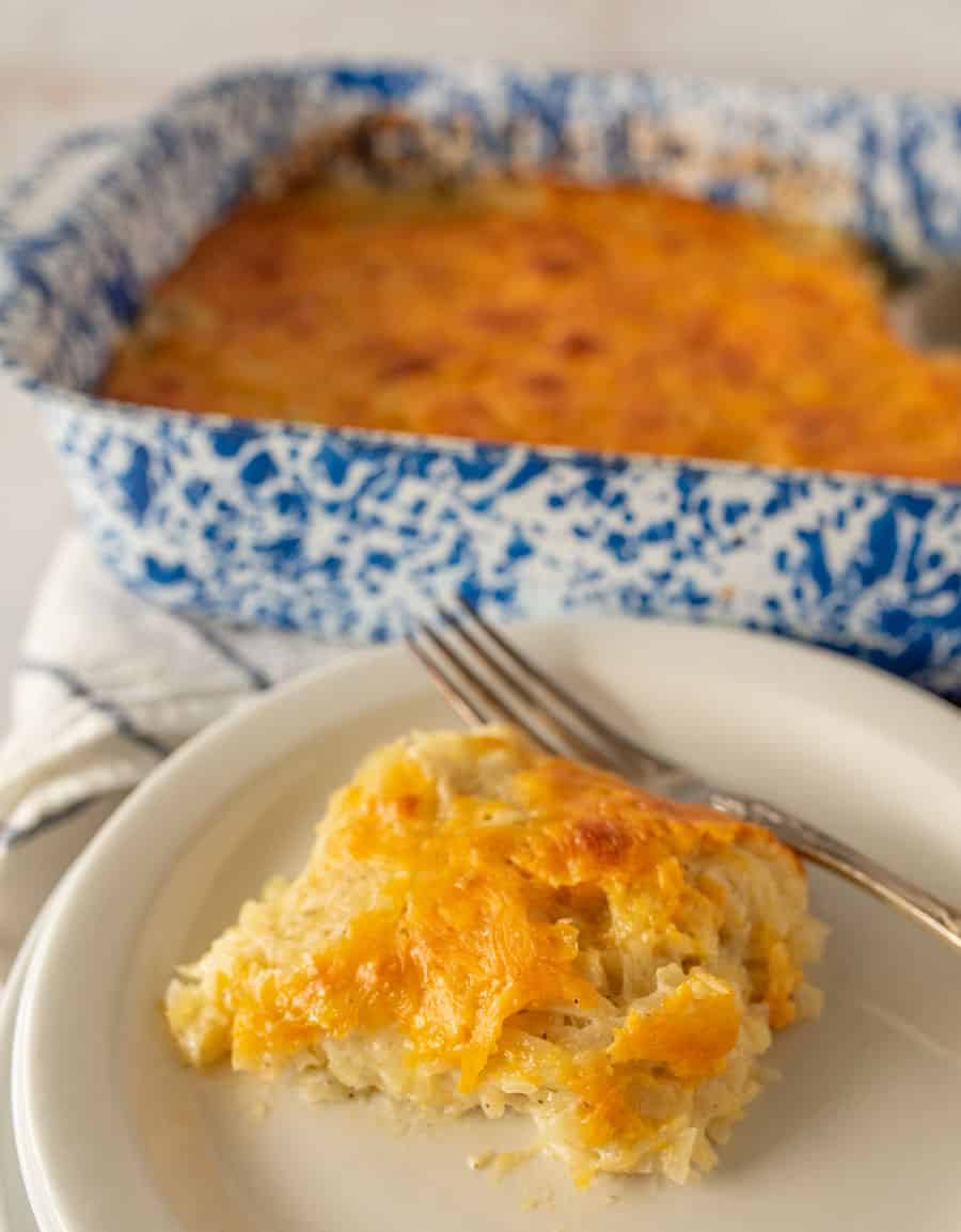 cheesy potato casserole on a plate with a fork and the baking dish in the back