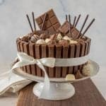 side view of chocolate candy cake with a ribbon around it on a cake stand