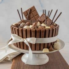 side view of chocolate candy cake with a ribbon around it on a cake stand