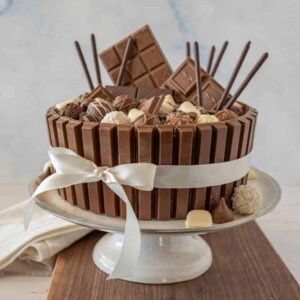 side view of chocolate candy cake with a ribbon around it on a cake stand