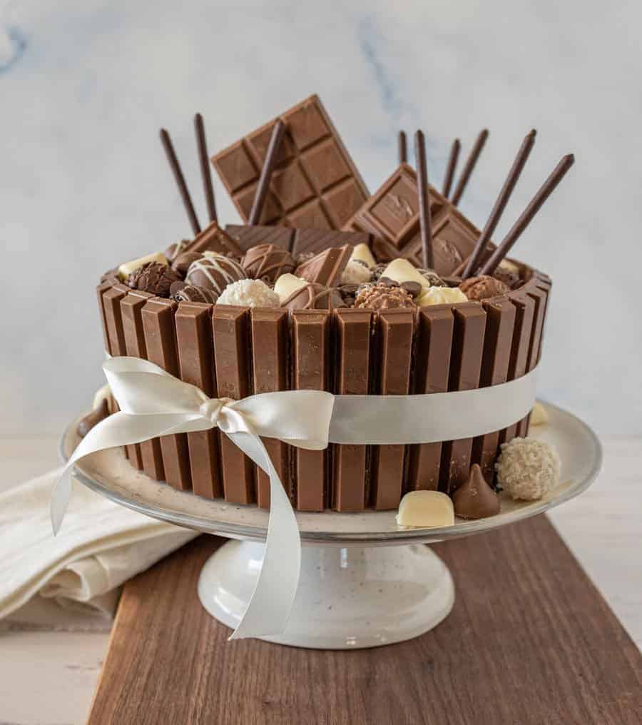 side view of chocolate candy cake with a ribbon around it on a cake stand