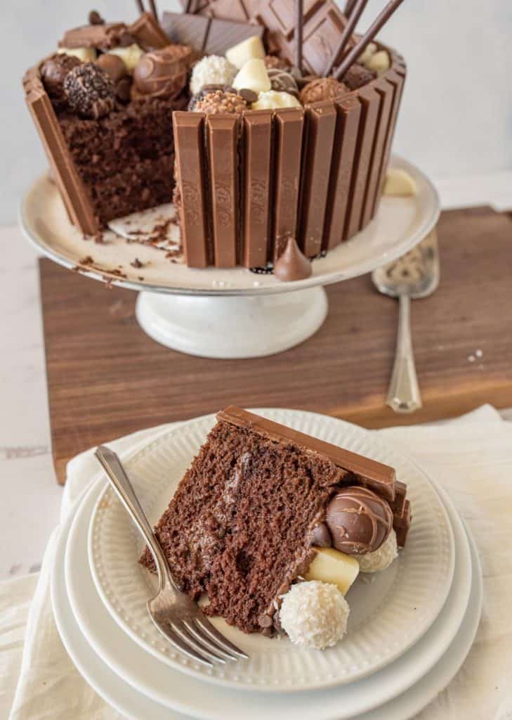 slice of chocolate candy cake on a plate with a fork and the rest of the cake in the background