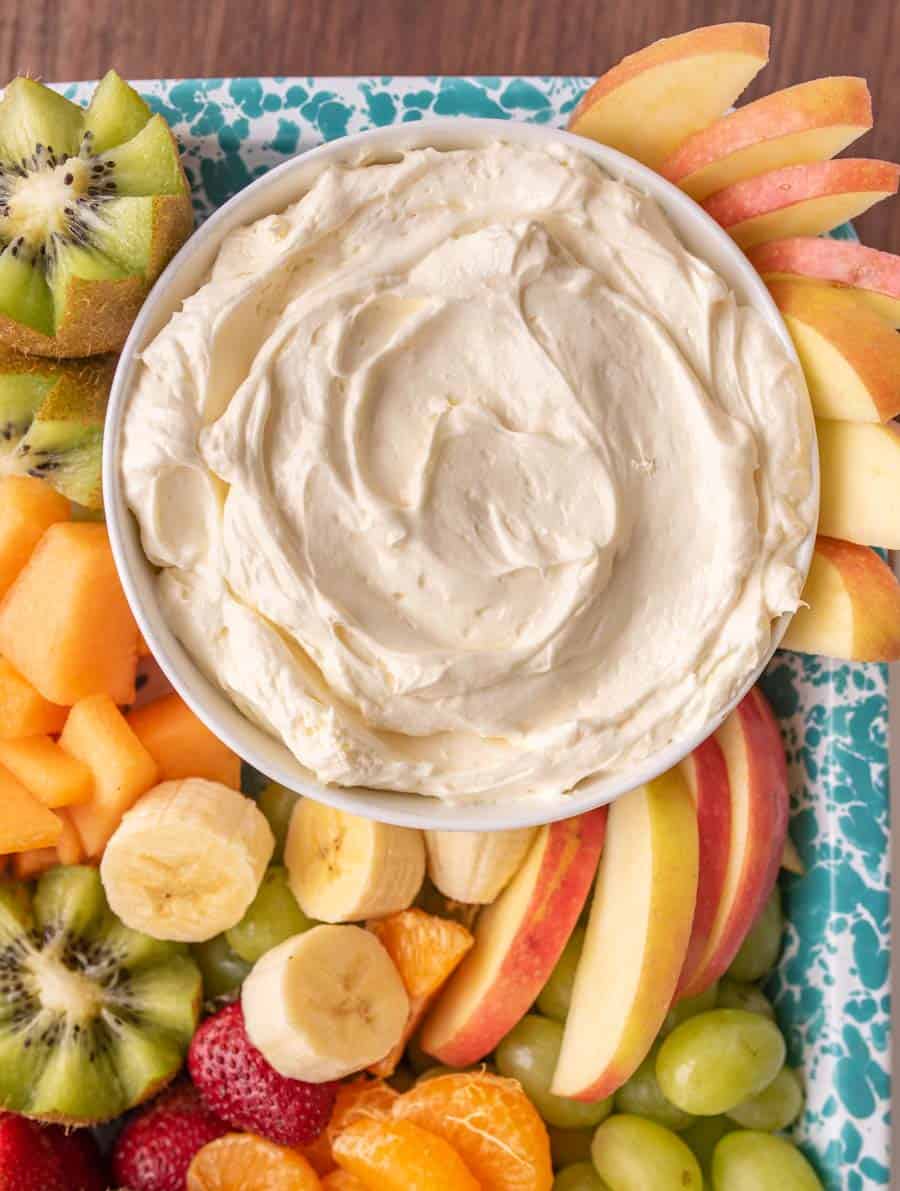 A close up view of a bowl of fluffy fruit dip surrounded by cut up fruit