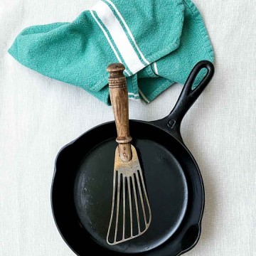 a cast iron pan with a fish spatula and a teal rag