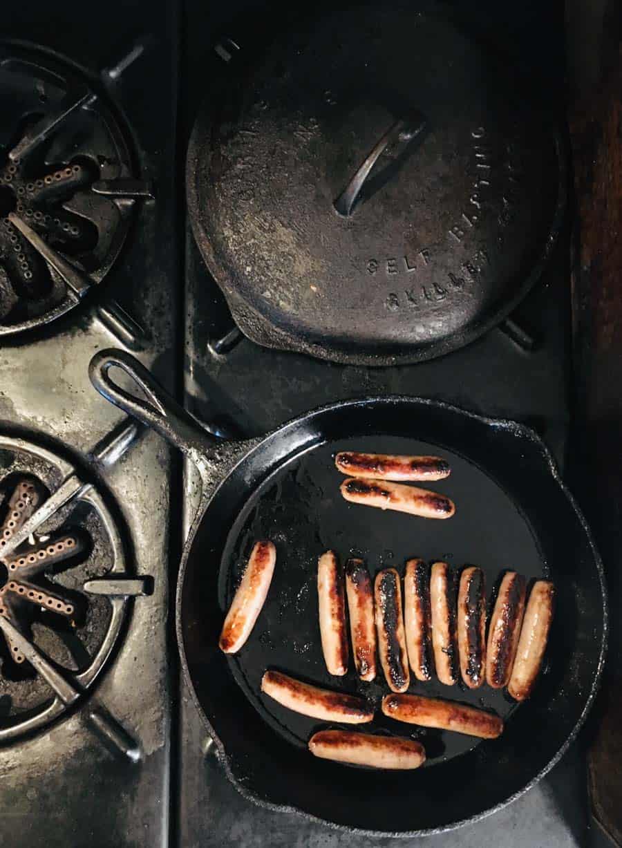 black cast iron skillet on black stove with cooked sausage links and grease in the skillet.