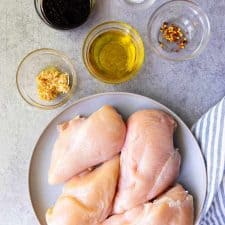 top view of a plate of chicken and ingredients for balsamic marinade in bowls next it