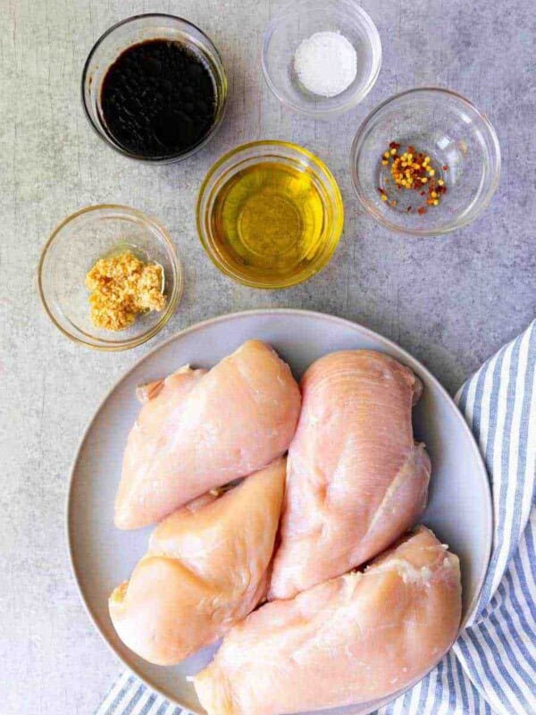 top view of a plate of chicken and ingredients for balsamic marinade in bowls next it