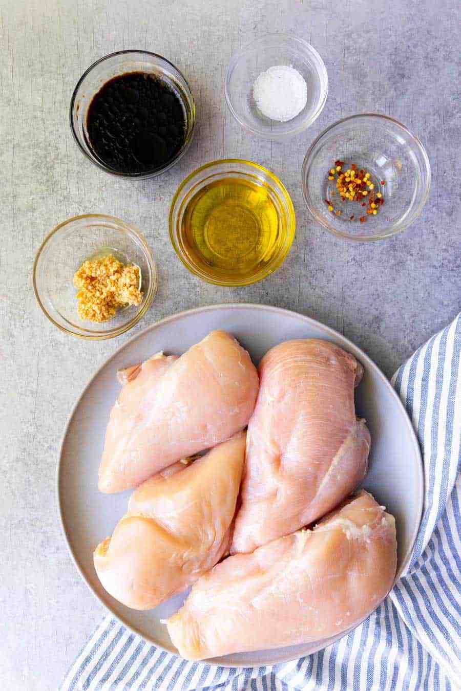 top view of a plate of chicken and ingredients for balsamic marinade in bowls next it