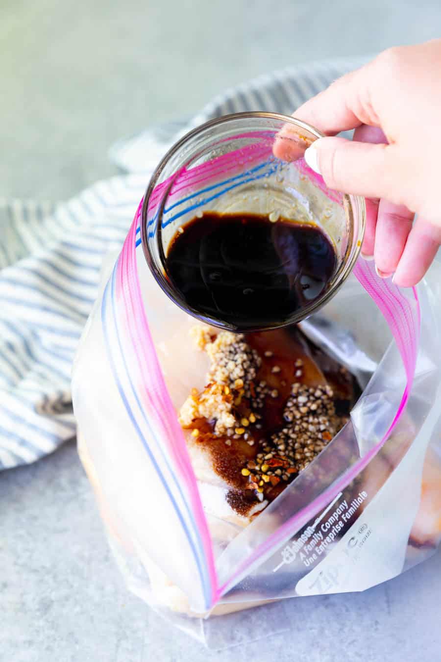 Balsamic marinade being poured into a bag of chicken.