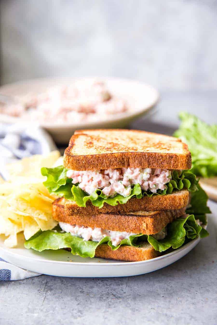 ham salad sandwiches stacked on a plate with chips