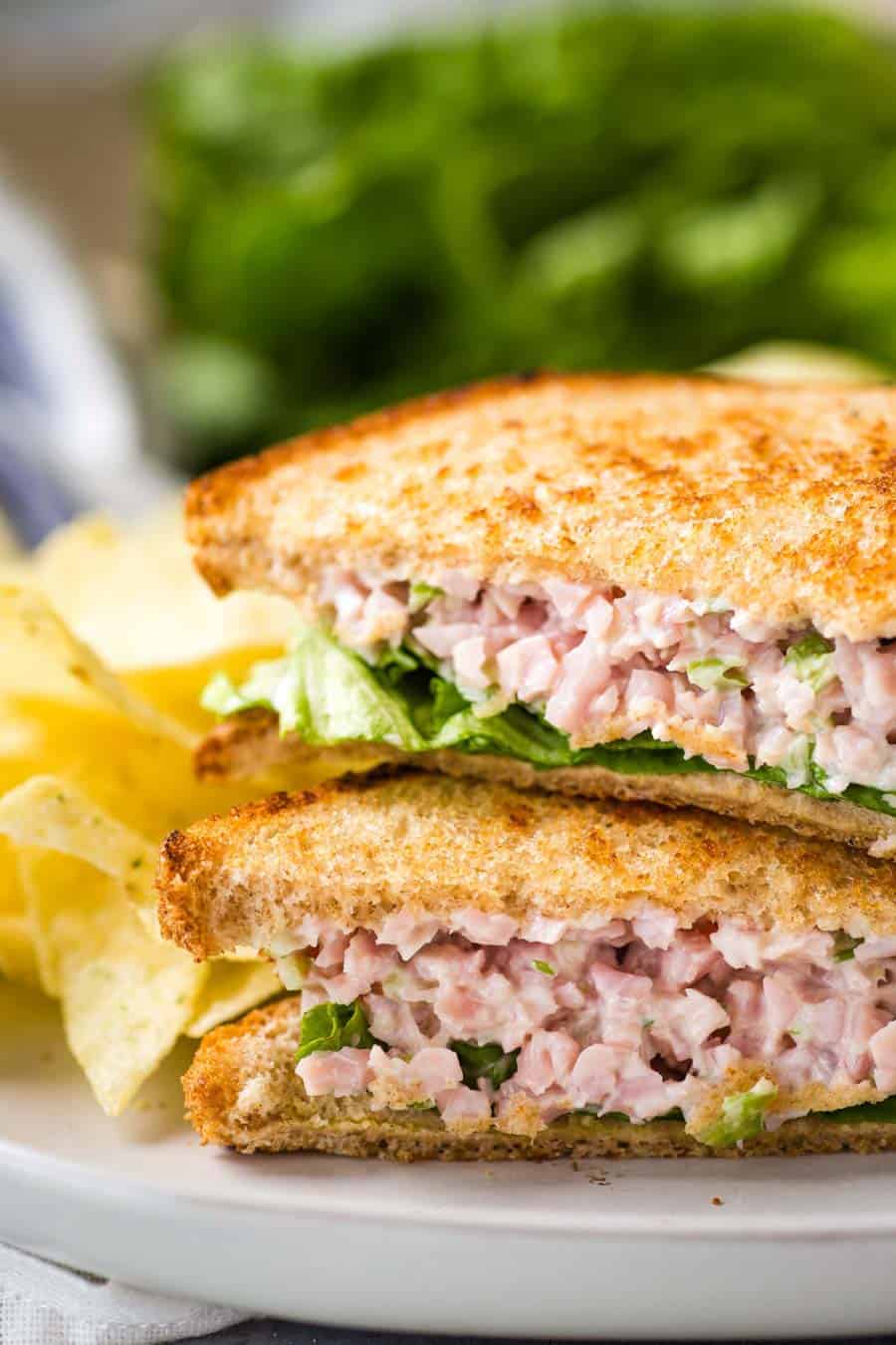 close up of ham salad sandwiches stacked on a plate with chips