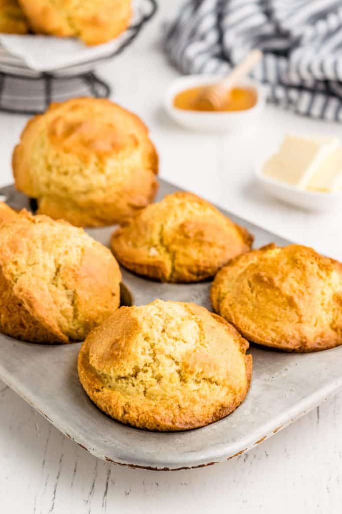 Cornbread muffins in muffin tin with honey and butter.