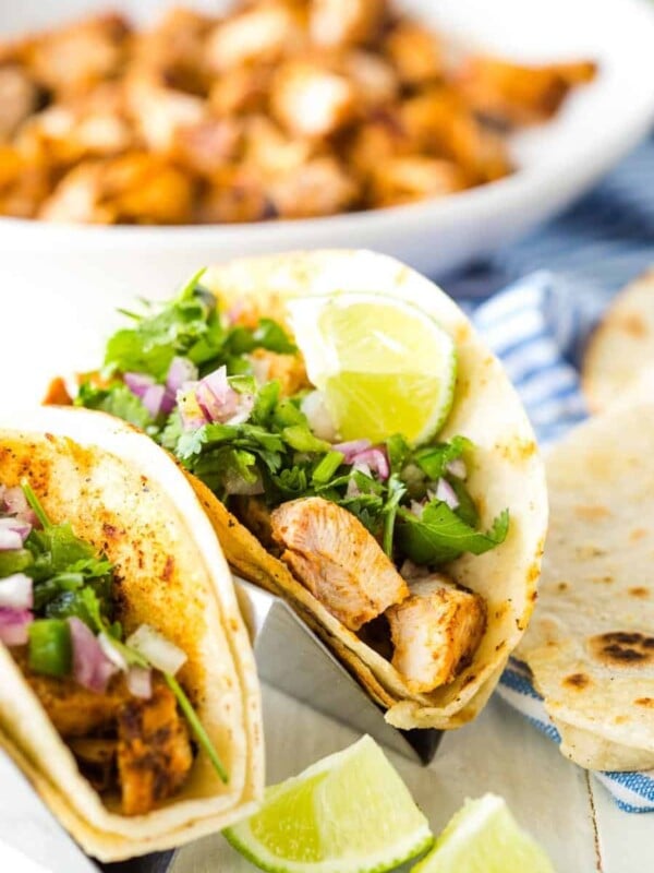 close up of chicken tacos with a bowl of chicken in the background