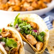 close up of chicken tacos with a bowl of chicken in the background