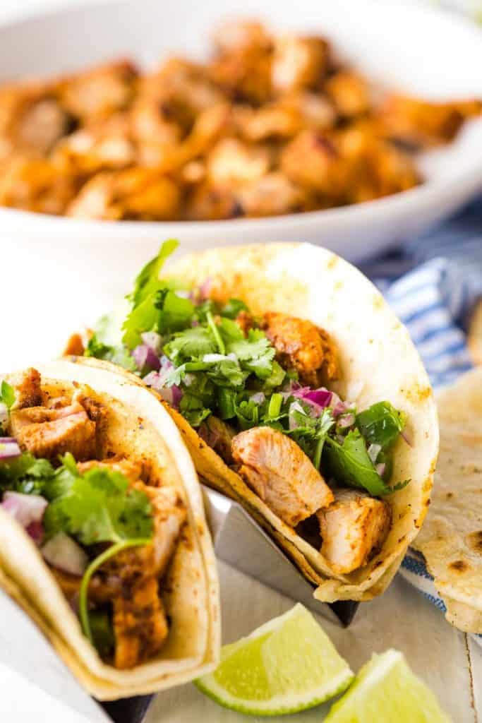close up of chicken tacos with a bowl of chicken in the background
