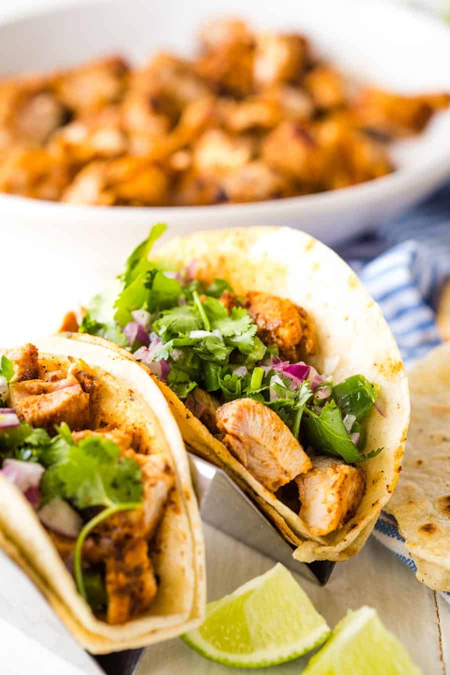 close up of chicken tacos with a bowl of chicken in the background
