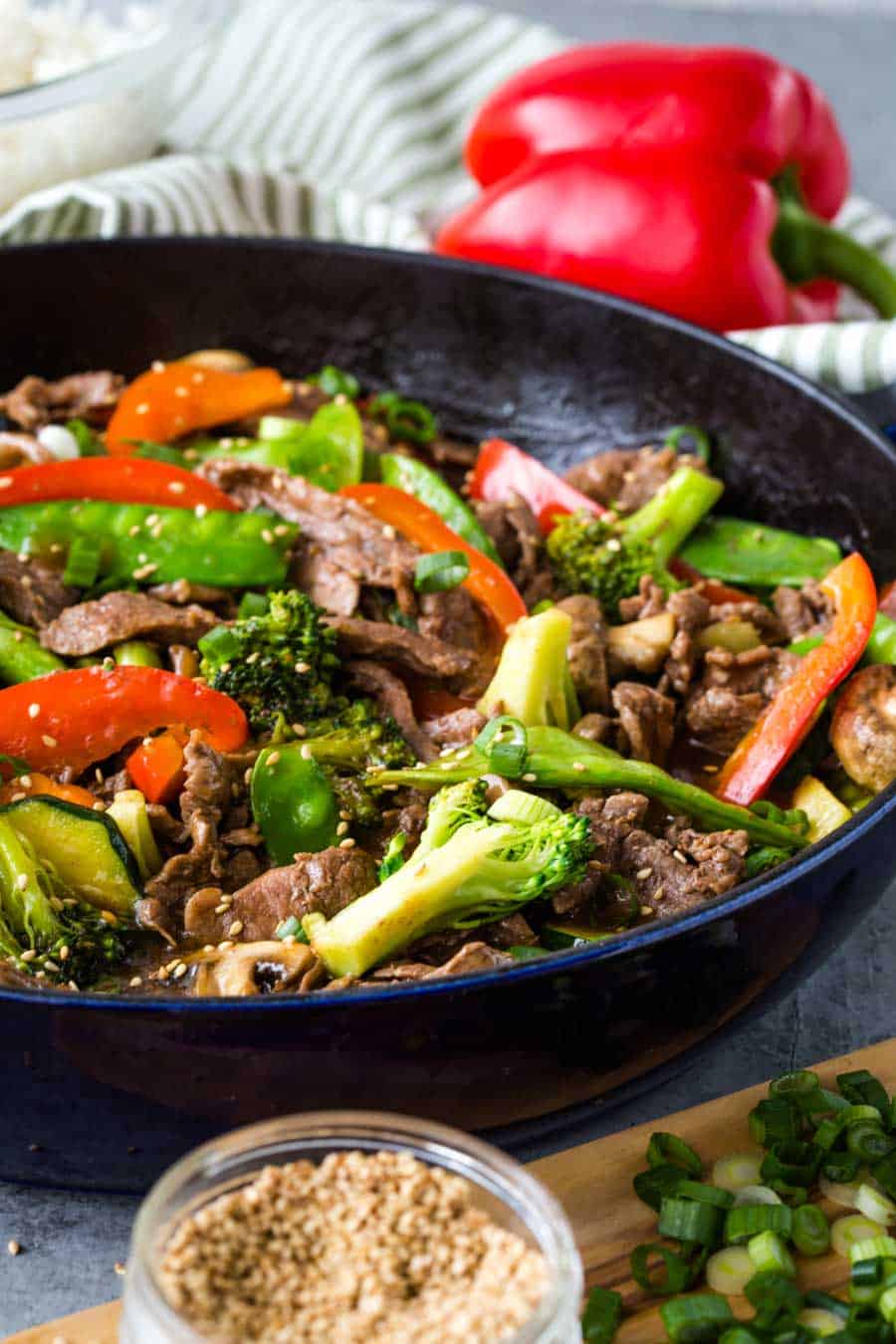 teriyaki beef and vegetables in a cast iron skillet with sesame seeds and green onions in foreground.