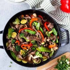 top view of teriyaki beef and vegetables with a towel, rice, and ingredients next to it