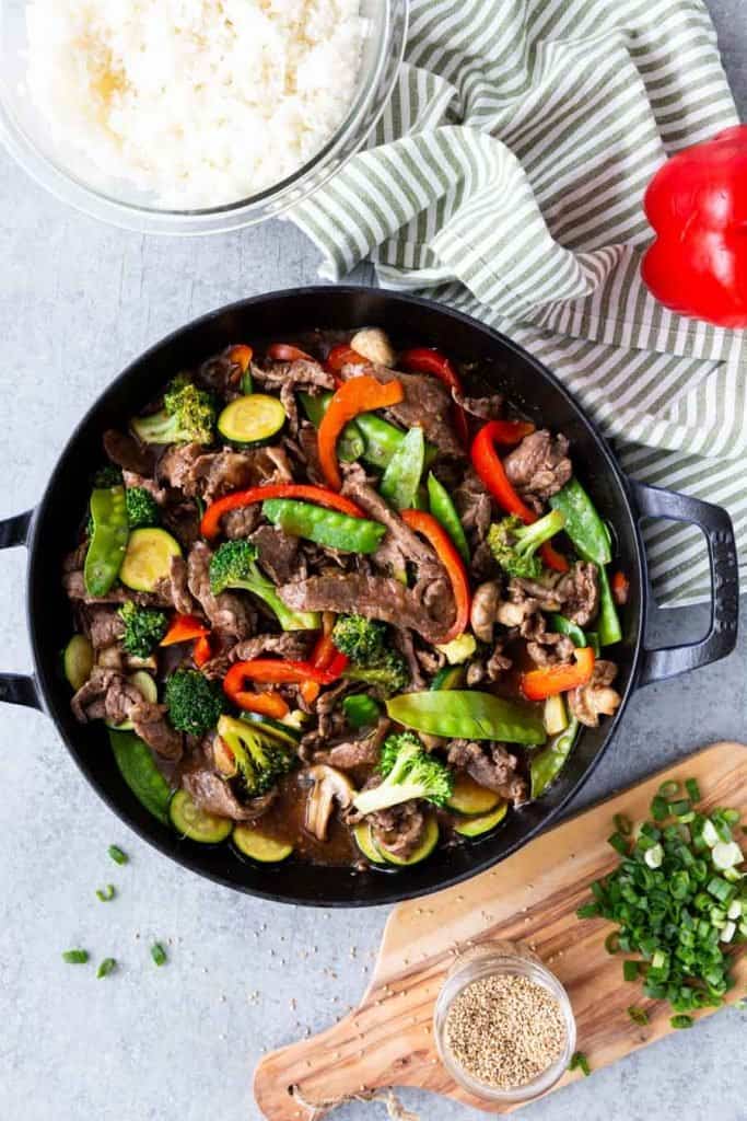 top view of teriyaki beef and vegetables with a towel, rice, and ingredients next to it