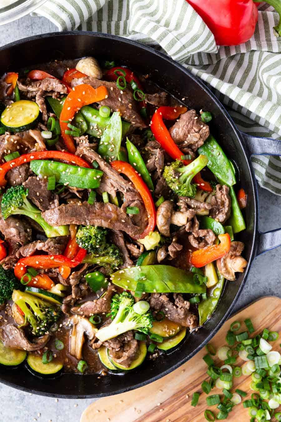 Top view of a skillet with beef, broccoli, bell peppers, snap peas, and sesame seeds.