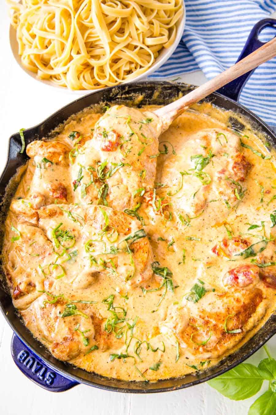 top view of Tuscan chicken in a skillet next to a bowl of pasta