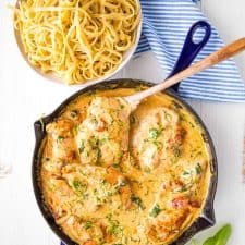 top view of Tuscan chicken in a skillet next to a bowl of pasta