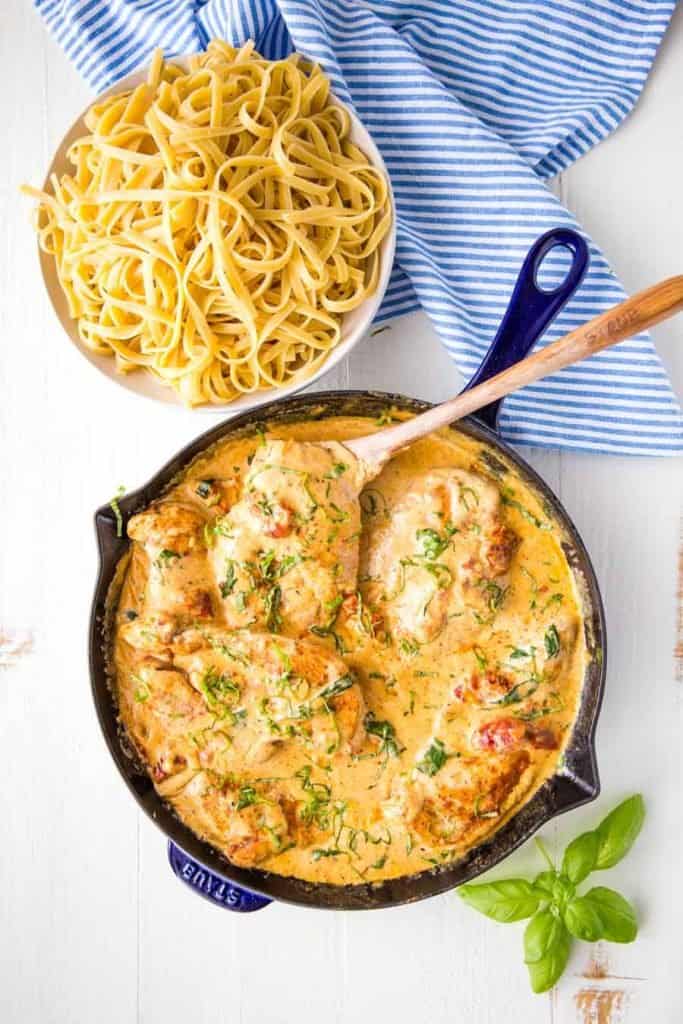 top view of Tuscan chicken in a skillet next to a bowl of pasta