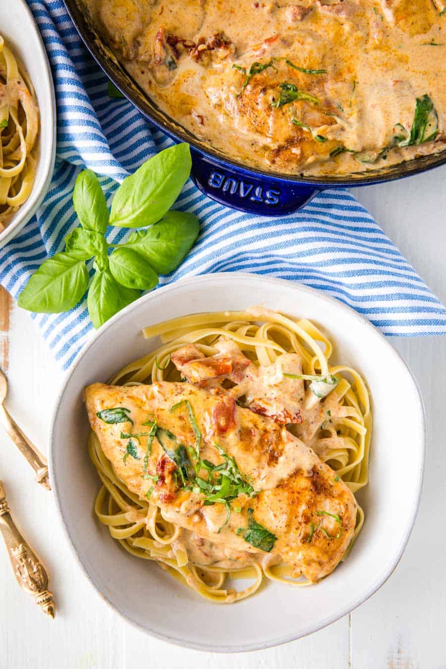 top view of tuscan chicken over pasta next to a cast iron skillet of the tuscan chicken