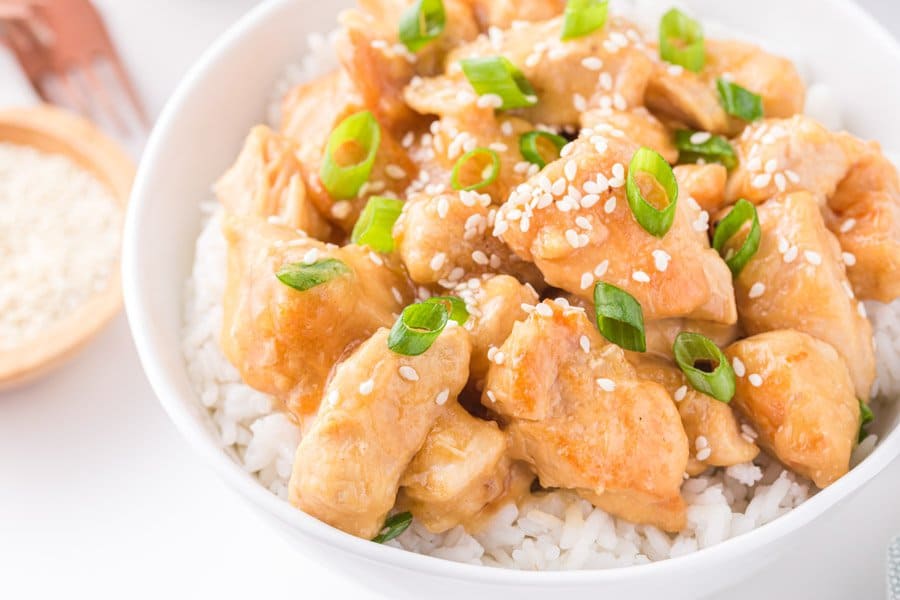 Top view of a white bowl with honey sesame chicken topped with sesame seeds and green onions.
