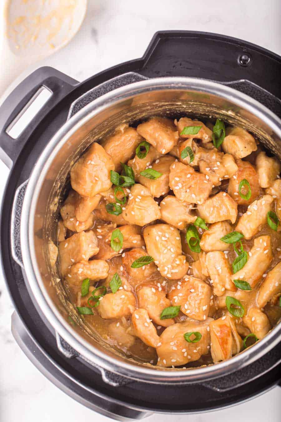 Top view of an InstaPot full of sesame chicken topped with green onion and sesame seeds.