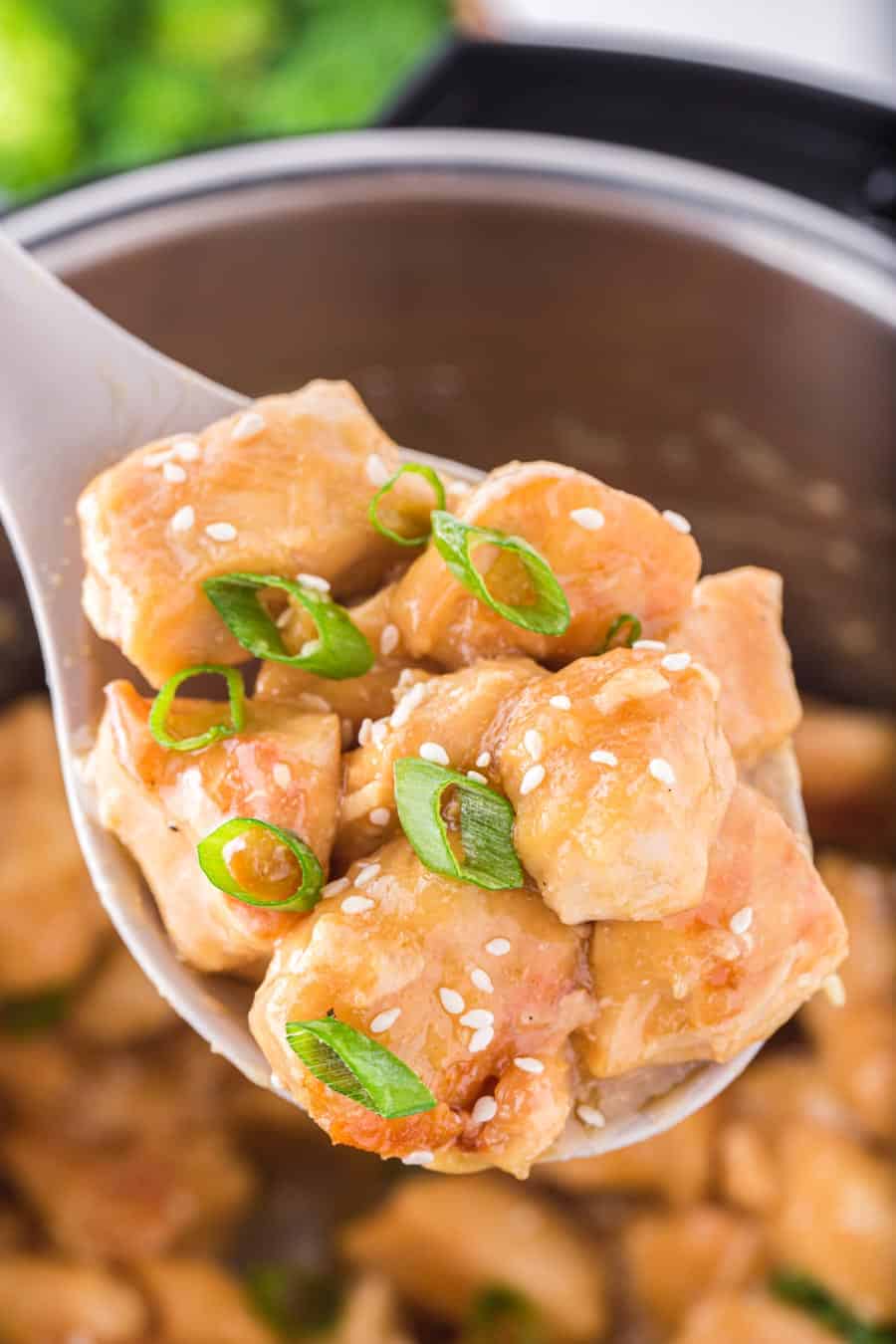 Close up of a spoon full of sesame chicken pieces with green onion and sesame seeds on top.