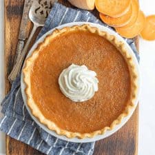 top view of sweet potato pie with whipped cream on top next to sliced sweet potato