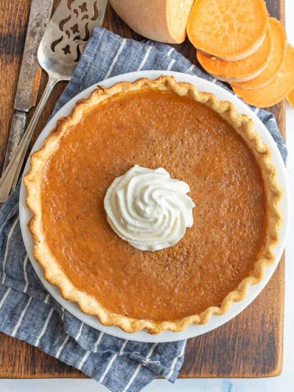 top view of sweet potato pie with whipped cream on top next to sliced sweet potato