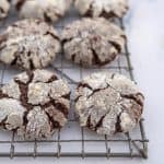 close up top view of a cooling rack cracked cookies that are nearly white on top but the cracks reveals dark chocolaty lines